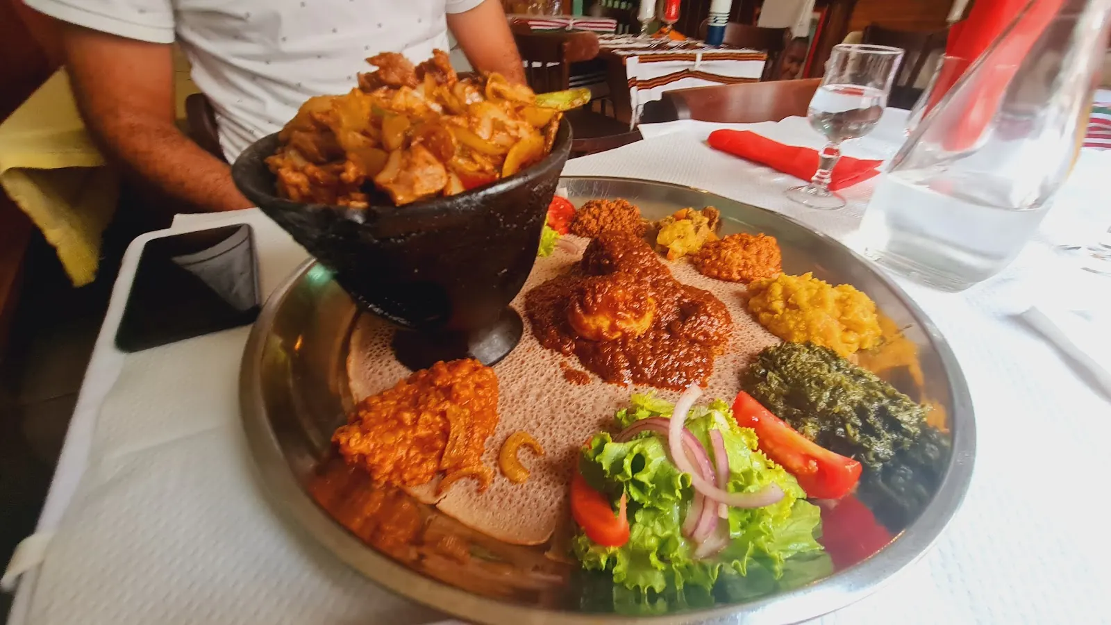 Plateau d'injera garni de ragoûts, avec un plat de tibs servi dans sa poêle en fonte